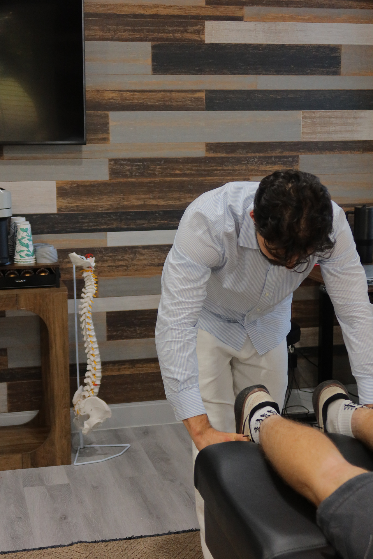 Dr. Rifati performing a leg-length check beside a spine model in the Refine office