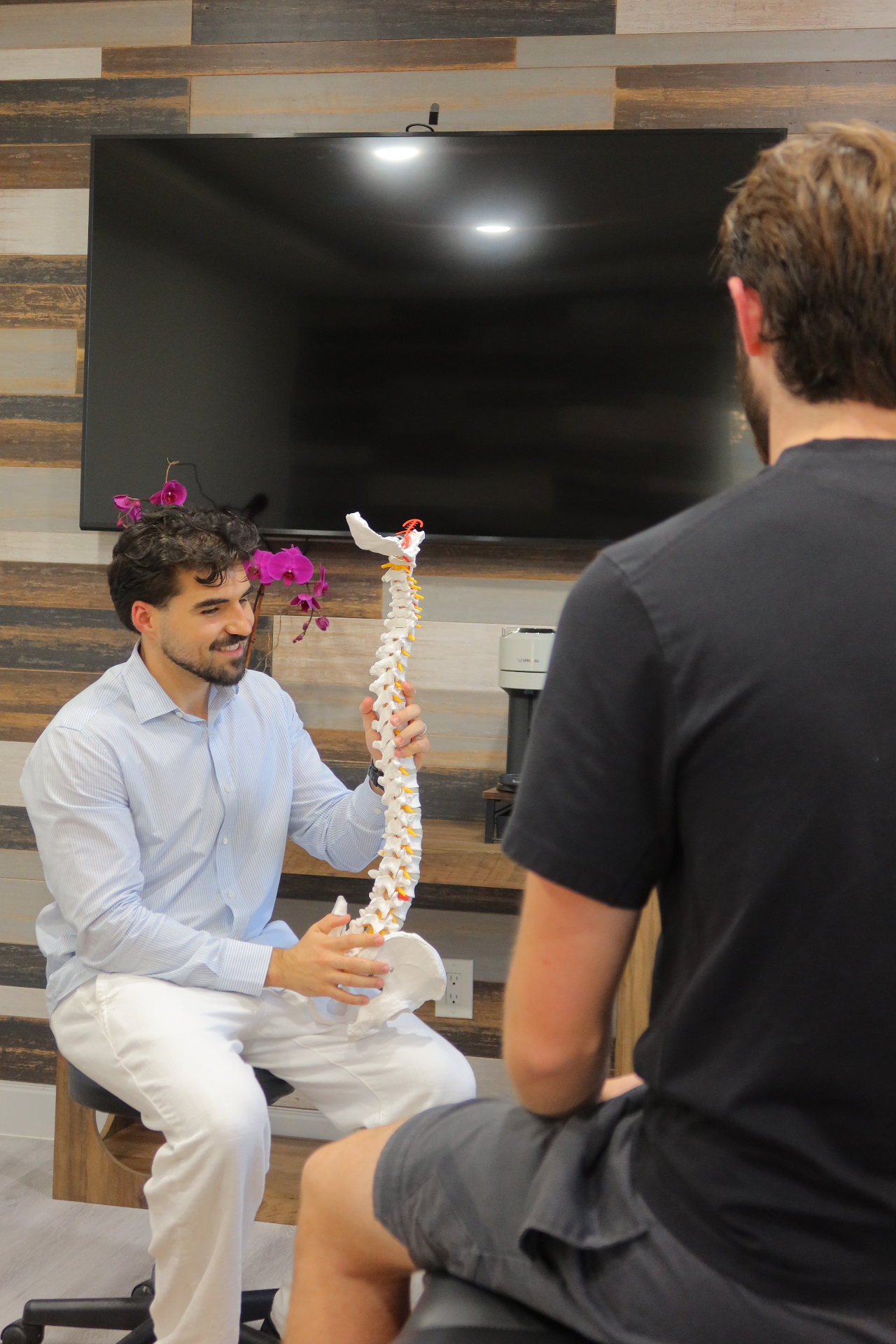 Portrait of Dr. Albir Rifati, DC explaining spinal anatomy to a patient at Refine Chiropractic